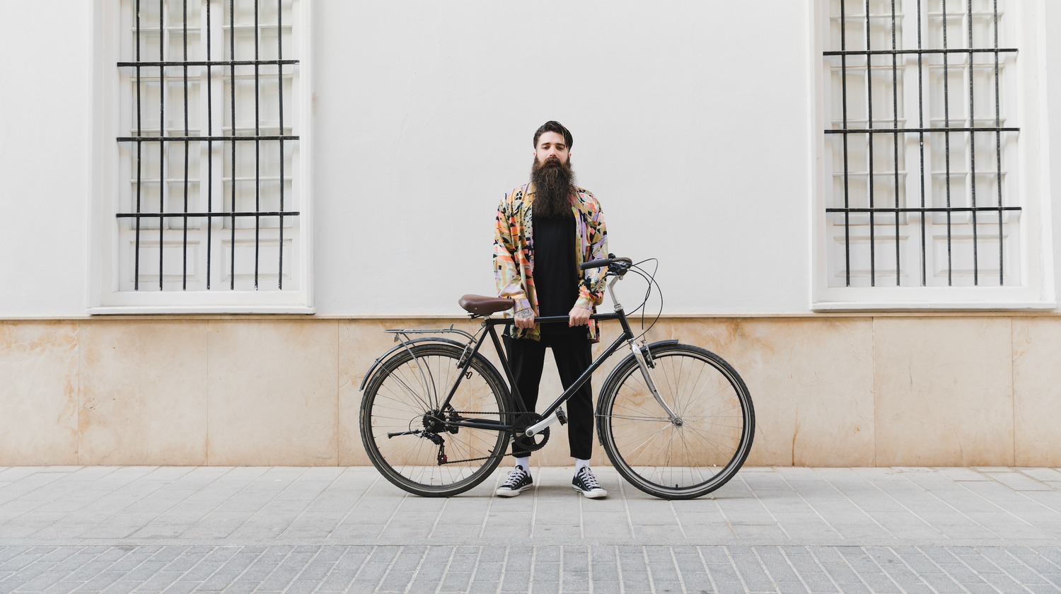 En man står och håller i sin elcykel med en byggnad i bakgrunden